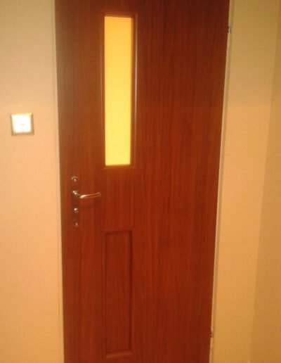 Bordowe drzwi do łazienki z wąskim pionowym oknem matowym