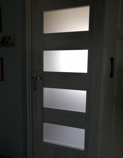 Białe drzwi z mlecznym przeszkleniem w ciemnym pomieszczeniu