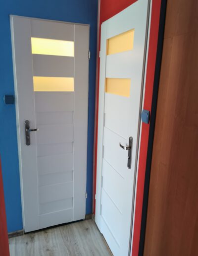 Białe drzwi z dwoma matowymi oknami zamontowane na kolorowych ścianach