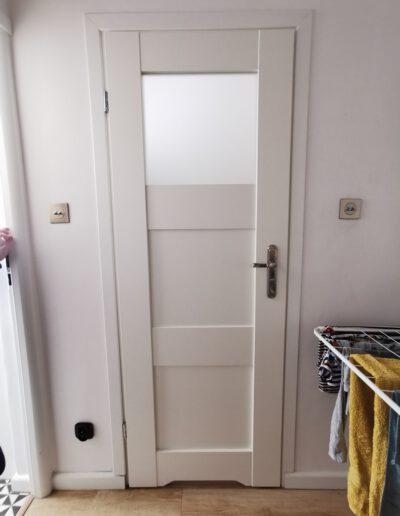 Białe drzwi do łazienki z otworem wentylacyjnym i matowym oknem