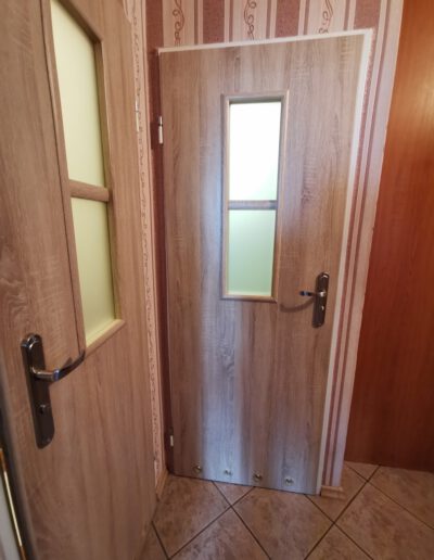 Realizacja instalacji drzwi drewnianych w holu z matowymi oknami